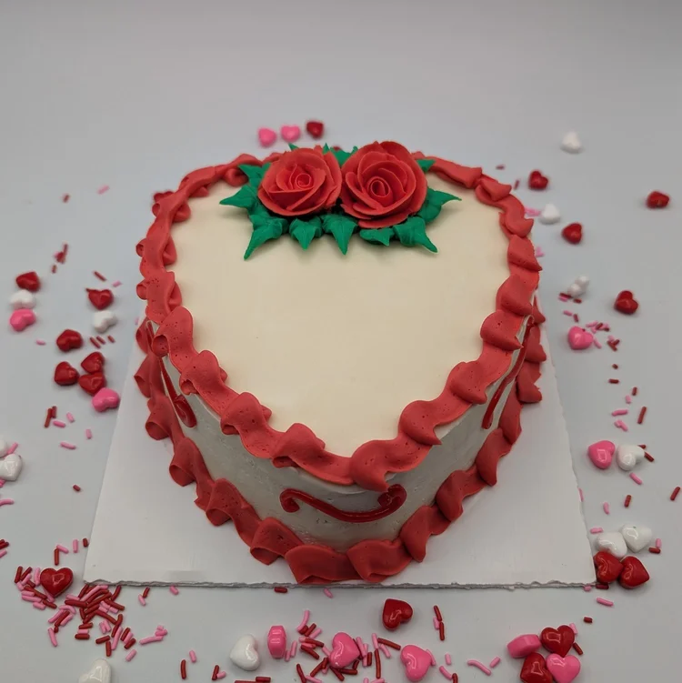 Heart-shaped ice cream cake with two red icing roses and red piped borders, surrounded by heart sprinkles, at Merla-Mae Ice Cream in London, Ontario