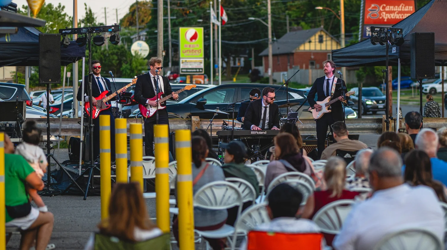 Live band performing for a seated crowd at the National Ice Cream Day concert at Merla-Mae Ice Cream in London, Ontario