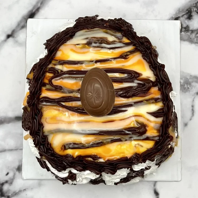 Egg-shaped ice cream cake swirled in white and orange with a piped chocolate border, chocolate drizzle and a chocolate egg on top, at Merla-Mae Ice Cream in London, Ontario