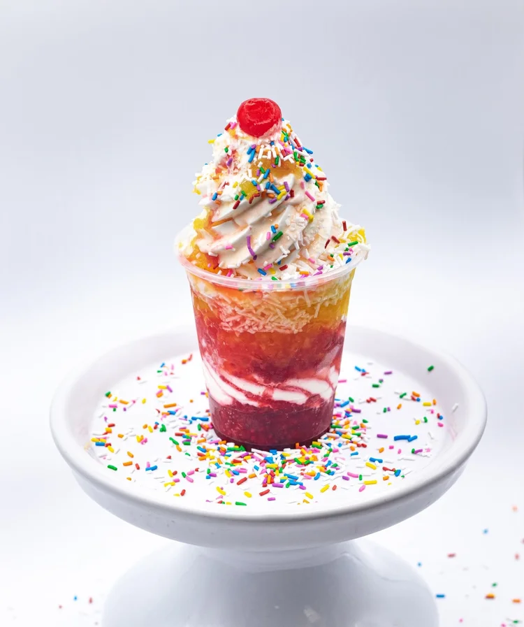 Layered parfait in a clear cup with red and golden fruit layers, a creamy swirl, rainbow sprinkles and a cherry at Merla-Mae Ice Cream in London, Ontario