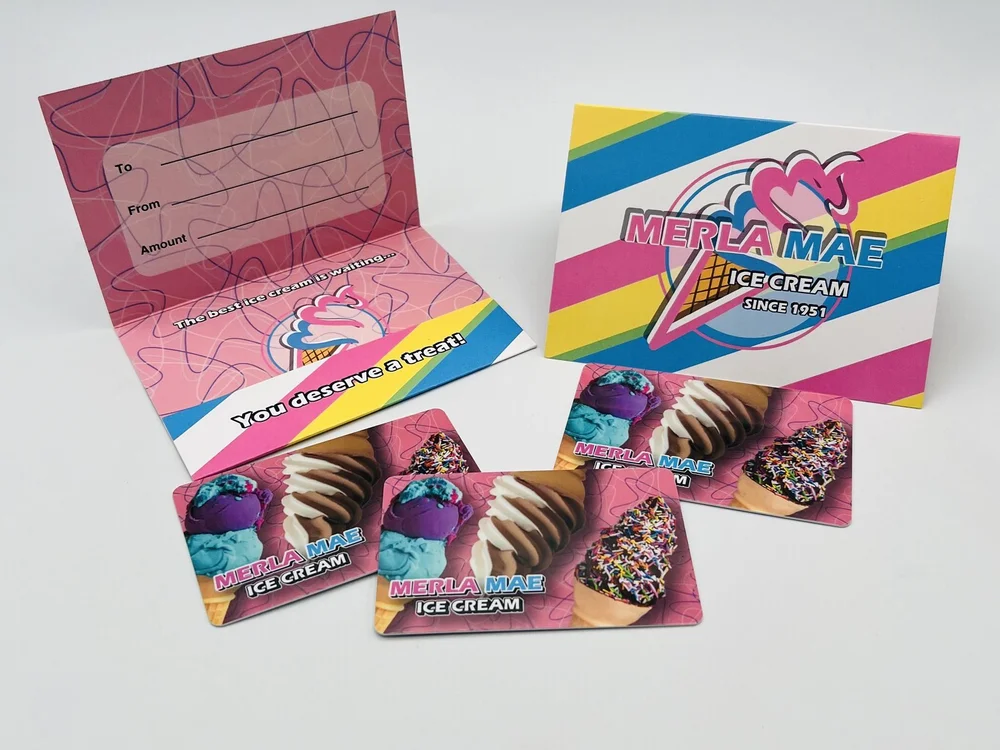 Three Merla-Mae gift cards in front of an open pink gift holder with To, From and Amount lines and a striped Merla-Mae holder, at Merla-Mae Ice Cream in London, Ontario