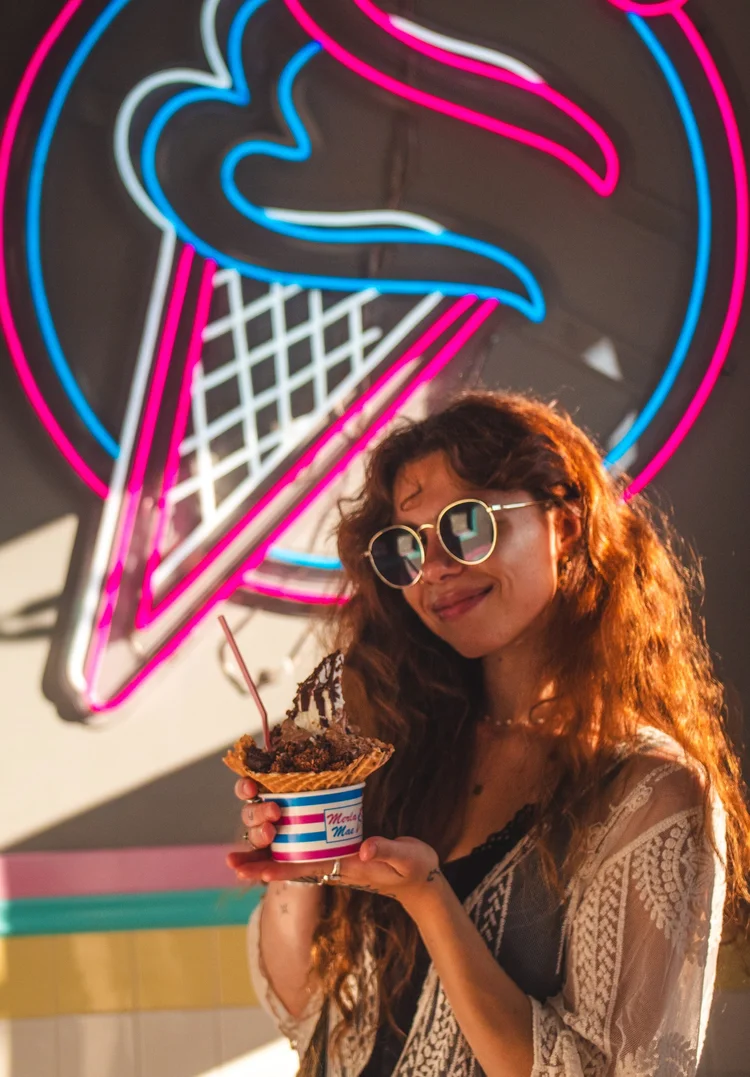 Francesca Panetta with a sundae in a striped Merla-Mae cup under the neon cone sign at Merla-Mae Ice Cream in London, Ontario