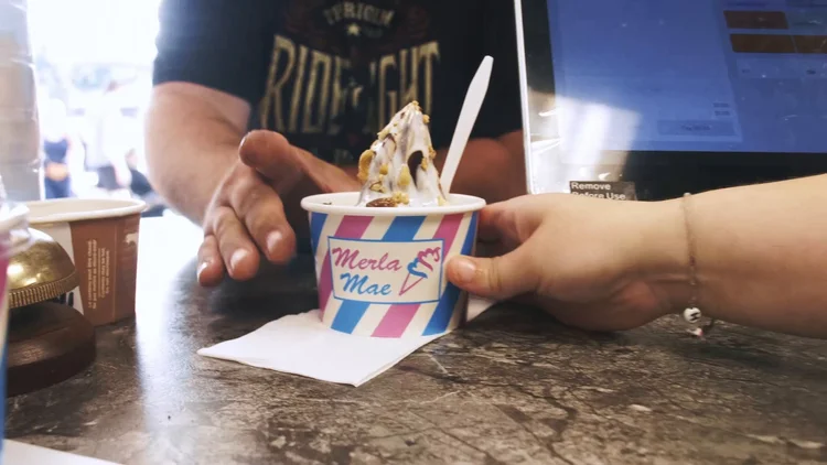 Soft-serve in a striped Merla-Mae cup handed across the counter at National Ice Cream Day 2024 in London, Ontario