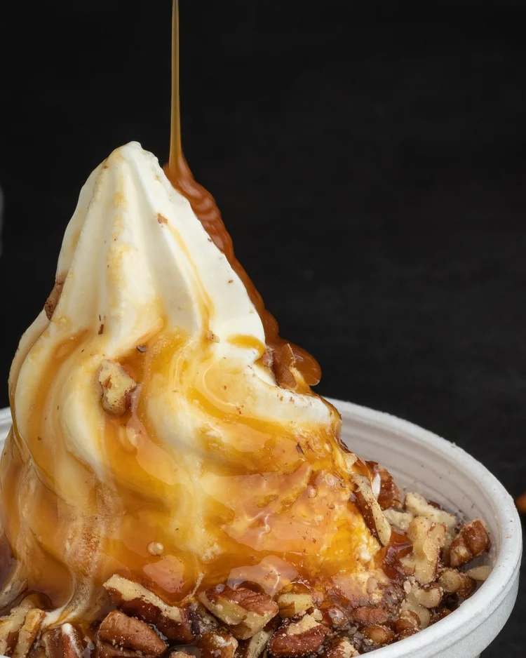 Close-up of hot caramel pouring onto a Caramel Cabaret soft-serve sundae with chopped pecans at Merla-Mae Ice Cream in London, Ontario