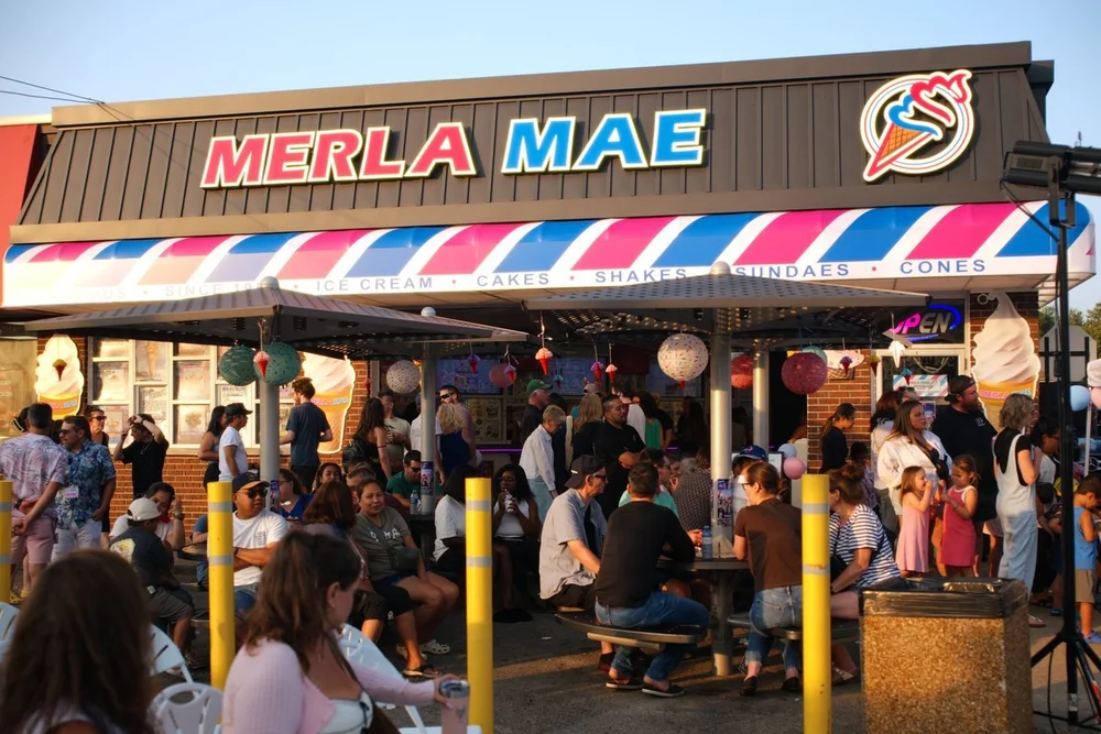 Crowd of guests on the patio under the Merla-Mae sign and striped awning during National Ice Cream Day in London, Ontario