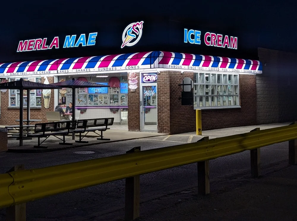 Merla-Mae Ice Cream lit up at night on Adelaide Street North in London, Ontario, with its striped awning, walk-up windows and patio tables under umbrellas