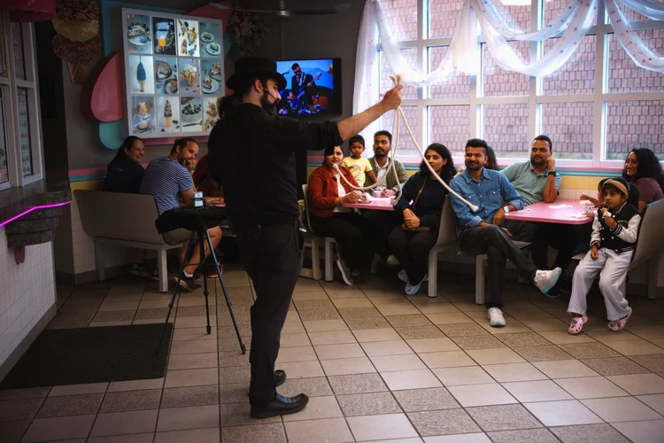 A magician performing a rope trick for families seated in the booths inside Merla-Mae Ice Cream during Magician Weekend in London, Ontario