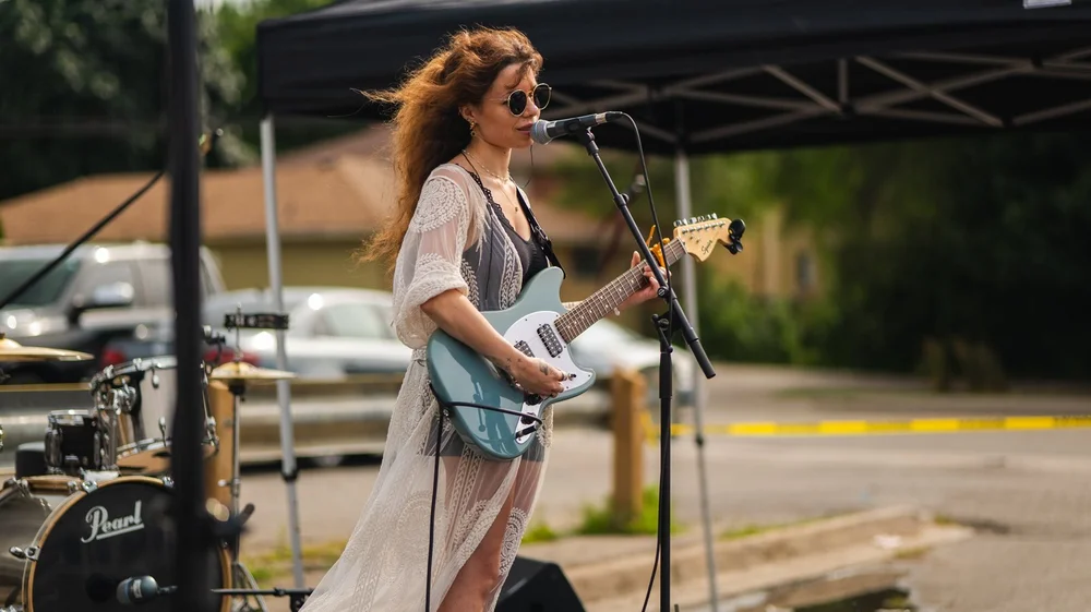 Francesca Panetta singing and playing electric guitar on the outdoor stage at National Ice Cream Day 2025, Merla-Mae Ice Cream in London, Ontario