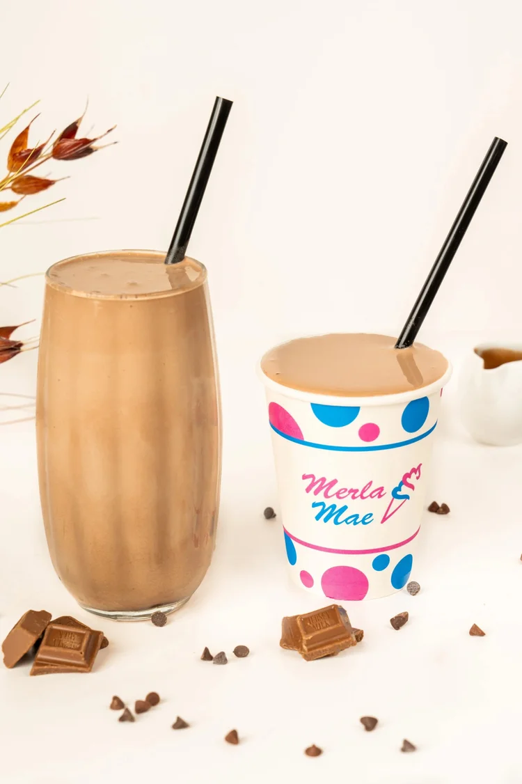 Chocolate milkshake in a tall glass and a polka-dot cup with chocolate pieces at Merla-Mae Ice Cream in London, Ontario