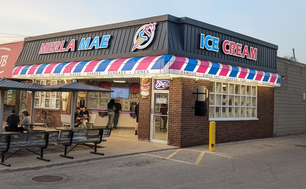 Merla-Mae Ice Cream storefront with its striped awning, open sign and outdoor tables on Adelaide Street North in London, Ontario