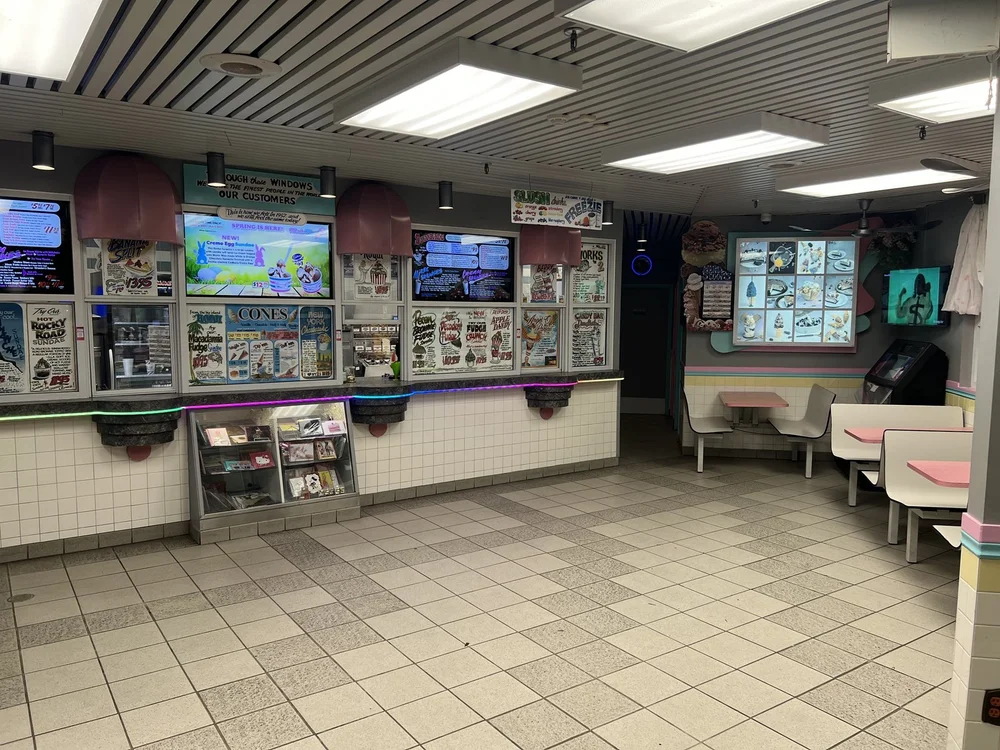 Inside Merla-Mae Ice Cream in London, Ontario: the order windows with menu boards and menu screens, and pink-and-white booths