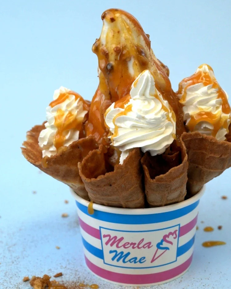 Apple Dandy sundae with soft-serve coated in hot caramel and cinnamon, topped with caramel-drizzled whipped cream, in a waffle dish set in a striped Merla-Mae cup at Merla-Mae Ice Cream in London, Ontario