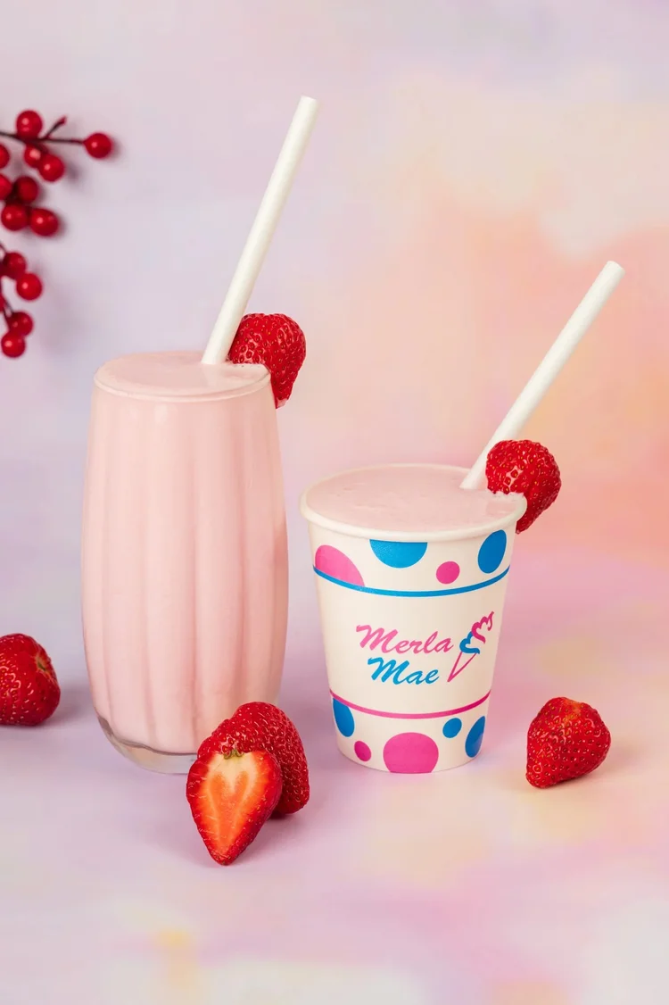 Strawberry milkshake in a tall glass and a polka-dot cup with fresh strawberries at Merla-Mae Ice Cream in London, Ontario