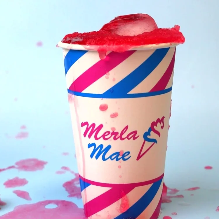 Red slush drink overflowing a pink and blue striped cup at Merla-Mae Ice Cream in London, Ontario