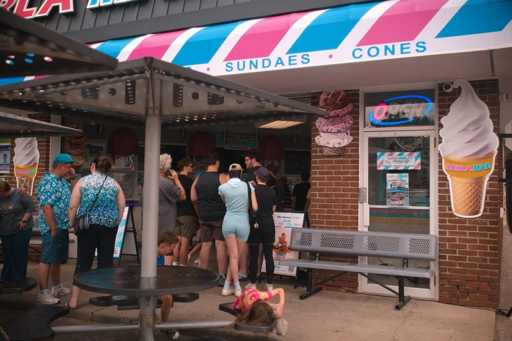 Families lining up at the outdoor order window under the striped Sundaes and Cones awning at Merla-Mae Ice Cream in London, Ontario