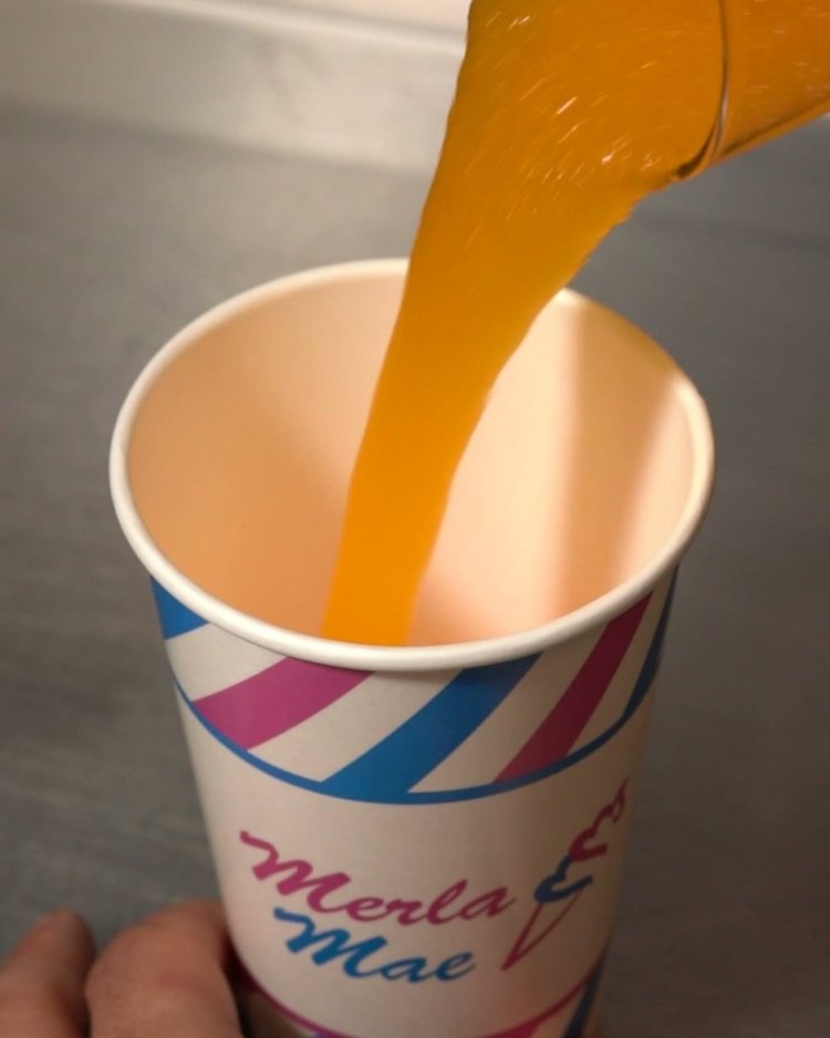 Orange slush being poured into a striped paper cup at Merla-Mae Ice Cream in London, Ontario