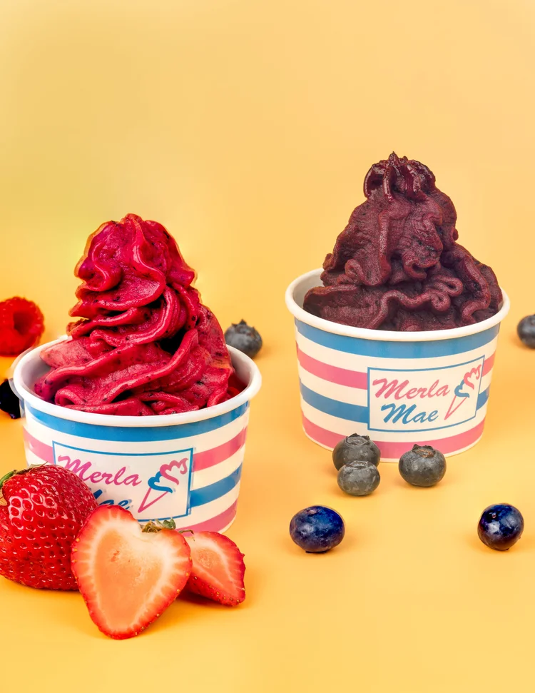Two cups of frozen yogurt, one bright pink and one deep purple, with fresh strawberries and blueberries at Merla-Mae Ice Cream in London, Ontario