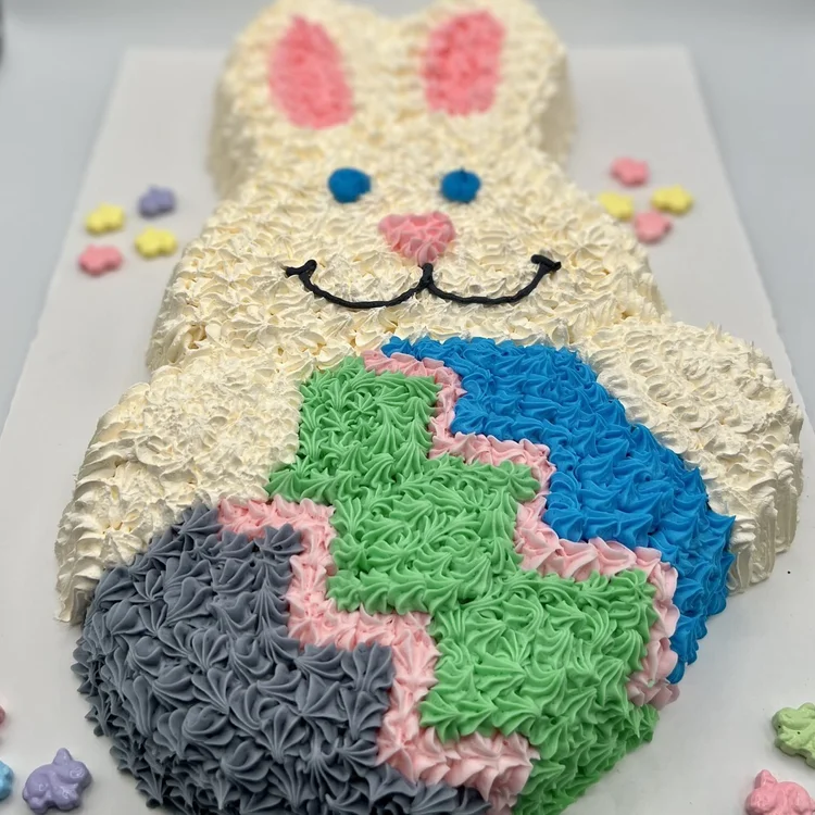 Bunny-shaped ice cream cake holding a painted Easter egg piped in green, blue, pink and grey, with pastel candy flowers on the board, at Merla-Mae Ice Cream in London, Ontario