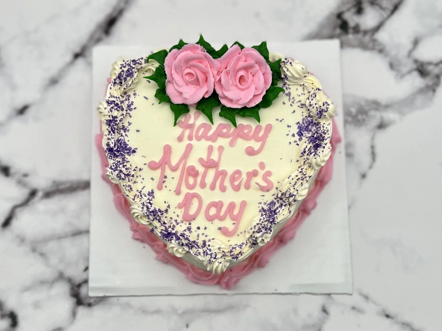 Heart-shaped ice cream cake piped with Happy Mother&rsquo;s Day in pink, topped with two pink icing roses and a purple sprinkle border, on white marble at Merla-Mae Ice Cream in London, Ontario