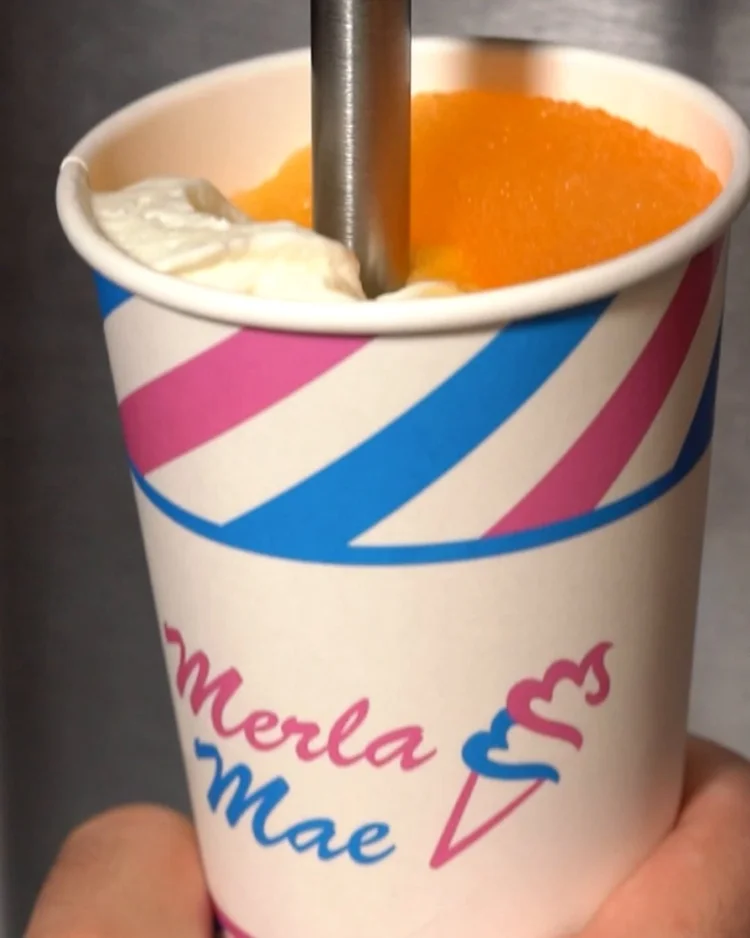 Spindle mixer blending orange slush and vanilla soft-serve in a striped cup at Merla-Mae Ice Cream in London, Ontario