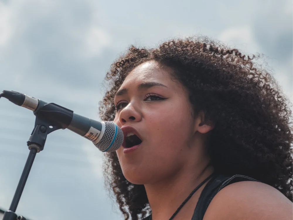Gianna Rigopoulos singing into the microphone on the outdoor stage at Merla-Mae Ice Cream in London, Ontario