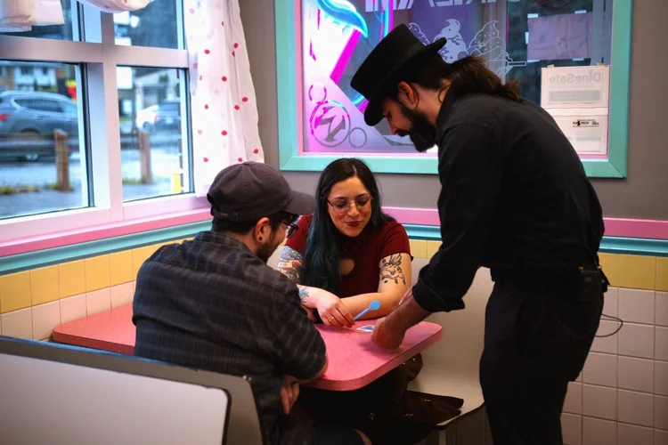 Magician performing a card trick for guests at a booth inside Merla-Mae Ice Cream