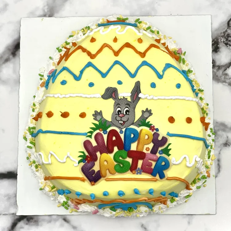 Yellow egg-shaped ice cream cake with orange, blue and white piped stripes, sprinkles and a Happy Easter bunny design, at Merla-Mae Ice Cream in London, Ontario