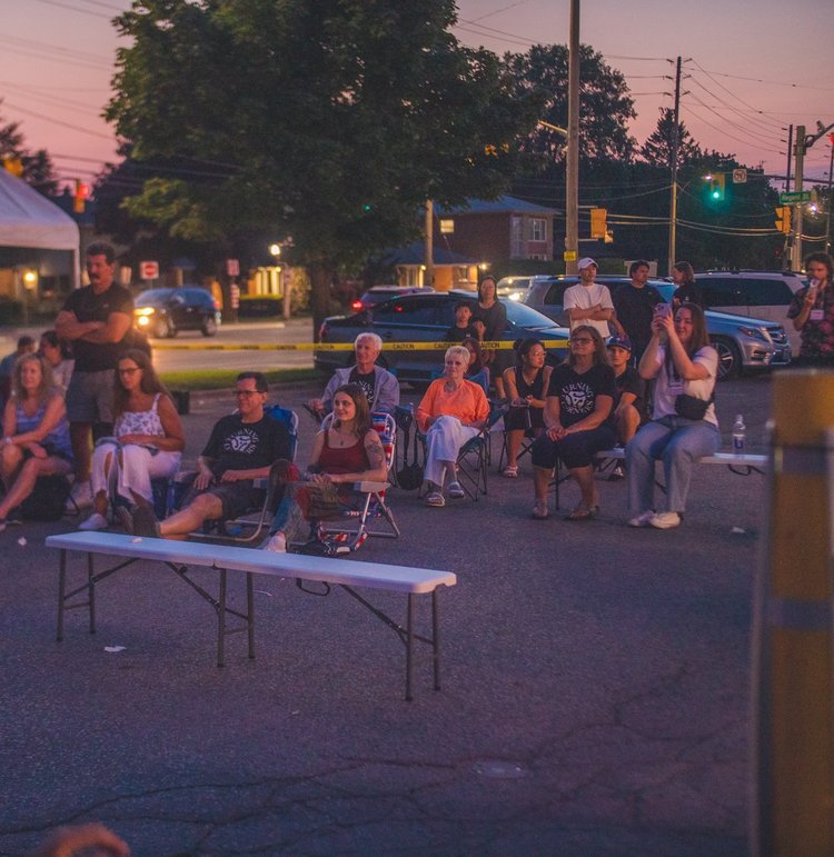 Audience in lawn chairs watching the evening set at dusk, National Ice Cream Day 2024 at Merla-Mae Ice Cream in London, Ontario
