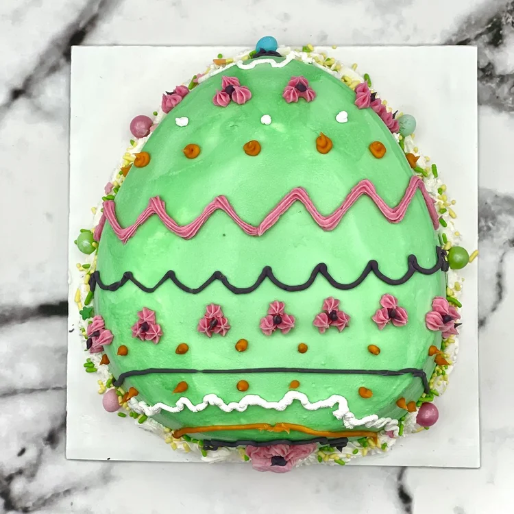 Green egg-shaped ice cream cake with pink and black piped zigzags, pink icing flowers, orange dots and sprinkles, at Merla-Mae Ice Cream in London, Ontario