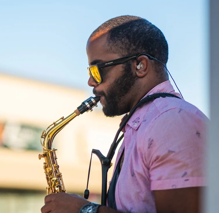 Saxophonist in Lyubov Kay's band playing against a blue sky at National Ice Cream Day 2025, Merla-Mae Ice Cream in London, Ontario
