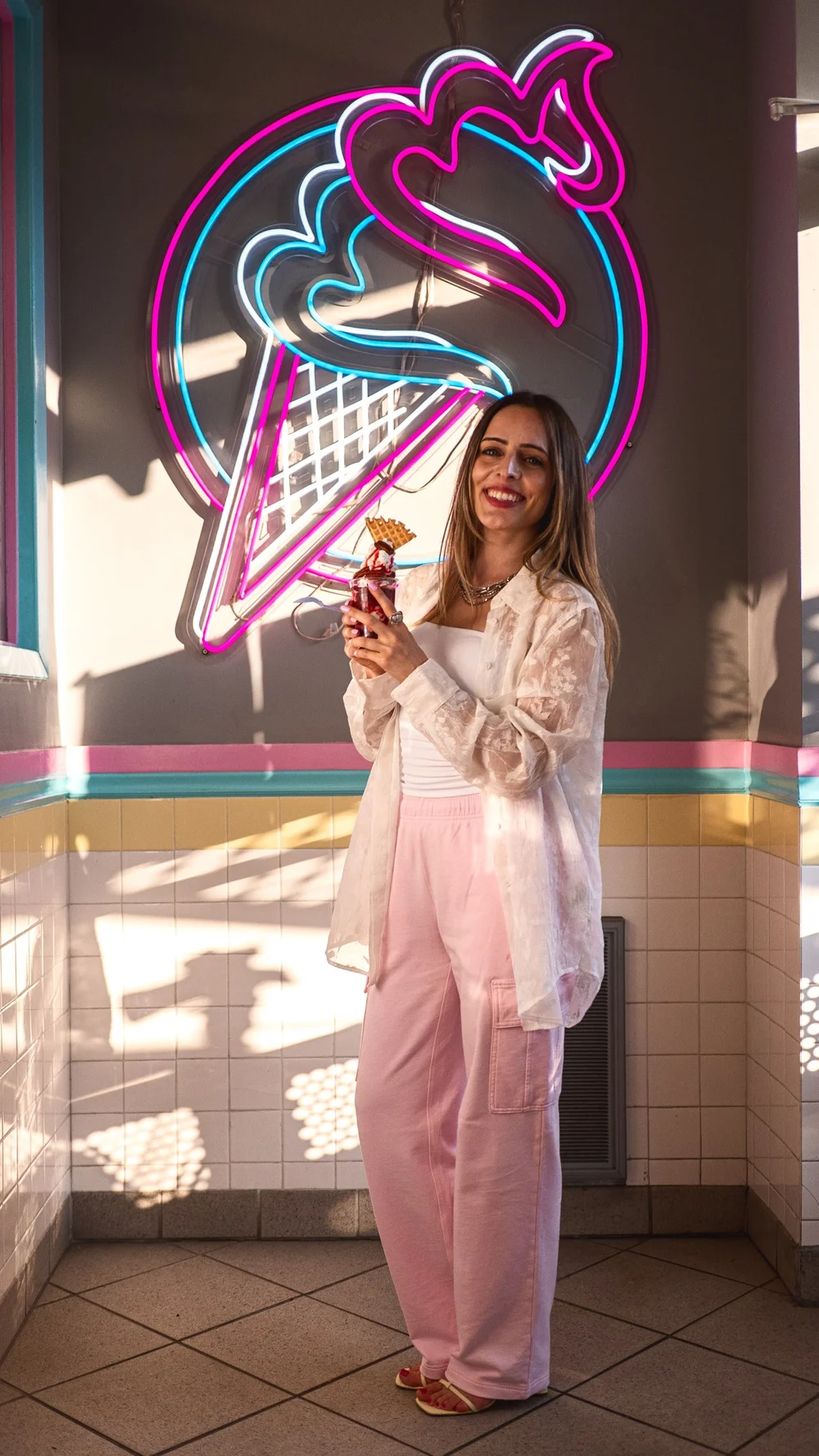 Lyubov Kay holding a raspberry parfait with a waffle wedge under the neon cone sign at Merla-Mae Ice Cream in London, Ontario