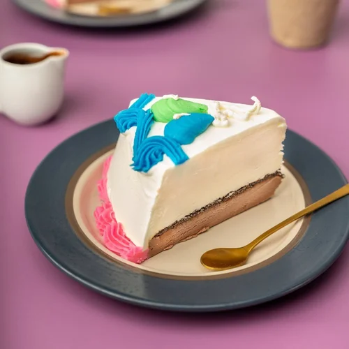 Slice of birthday ice cream cake with vanilla and chocolate layers, blue, green and pink piped icing, on a plate at Merla-Mae Ice Cream in London, Ontario