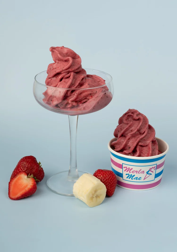 Pink strawberry and banana pressed fruit in a glass dish and a striped cup, with fresh strawberries and banana, at Merla-Mae Ice Cream in London, Ontario