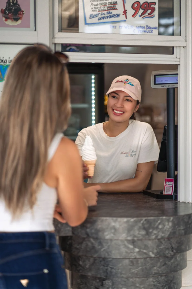 Merla-Mae team member in a pink cap handing a soft-serve cone to a customer at the order window in London, Ontario