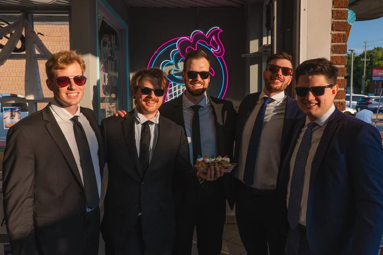 Turning Corners in suits and sunglasses with their signature sundae under the neon cone sign at Merla-Mae Ice Cream in London, Ontario