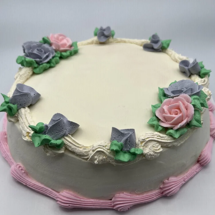Round ice cream cake with a smooth ivory top, piped pink and lavender-grey roses with green leaves around a cream shell border, and a pink piped bottom border, at Merla-Mae Ice Cream in London, Ontario