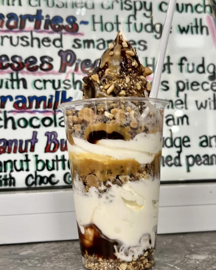 Peanut butter parfait with fudge, peanut butter and crushed peanuts in front of the hand-painted parfait menu at Merla-Mae Ice Cream in London, Ontario