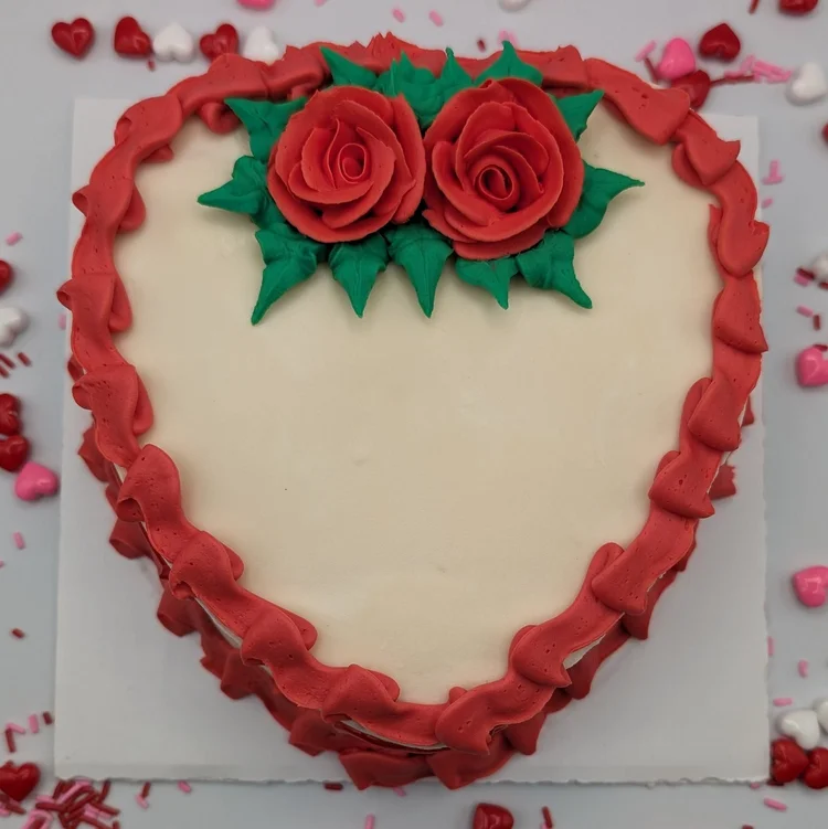Heart-shaped ice cream cake with a white top, two red piped roses and a red ruffled border, surrounded by heart candies and sprinkles, at Merla-Mae Ice Cream in London, Ontario
