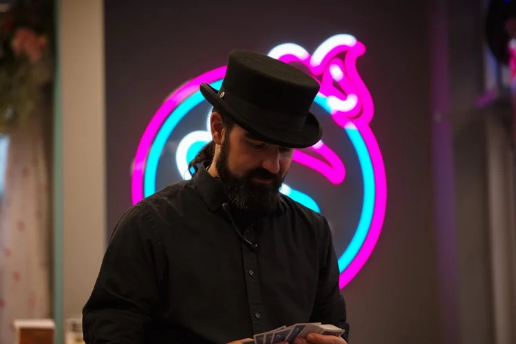 Magician shuffling cards beneath the neon ice cream cone sign at Merla-Mae Ice Cream