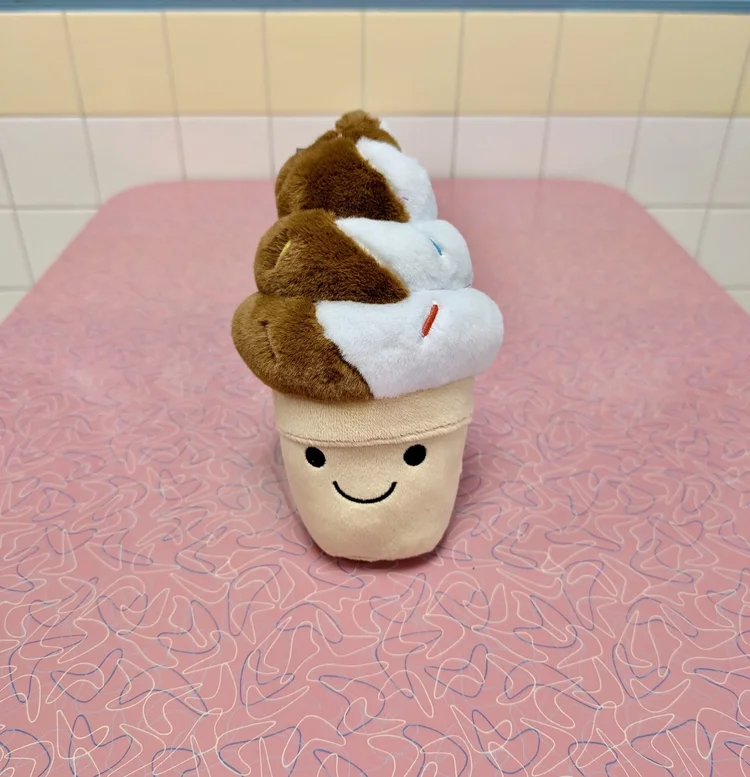 Soft-serve twist cone plushie with sprinkles and a smiling face on a pink boomerang table at Merla-Mae Ice Cream in London, Ontario
