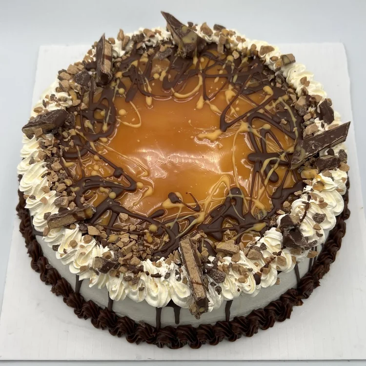 Round ice cream cake with a glossy caramel top, toffee bits, chocolate drizzle and chocolate bar pieces inside a whipped rosette border, at Merla-Mae Ice Cream in London, Ontario