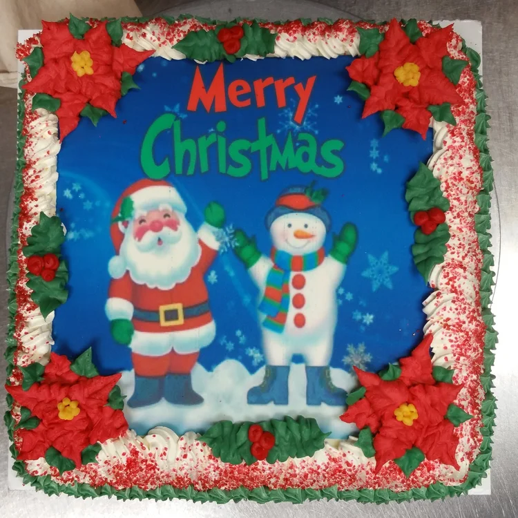 Square Christmas ice cream cake from above, with a printed Merry Christmas picture of Santa and a snowman, red icing poinsettias in each corner, holly and a red-sprinkled white border, at Merla-Mae Ice Cream in London, Ontario