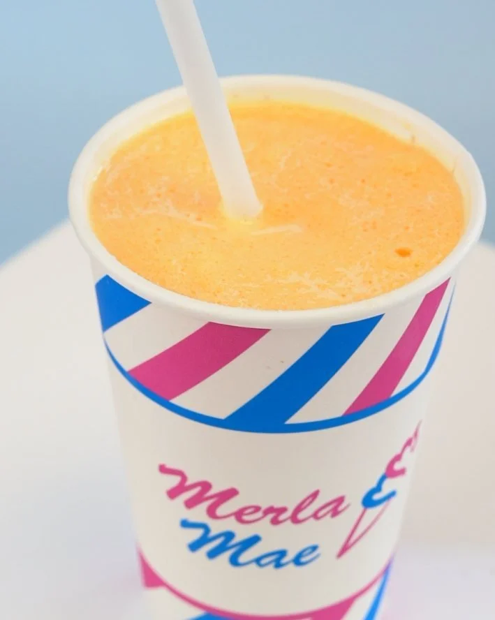 Orange Freezie with a straw in a striped Merla-Mae cup at Merla-Mae Ice Cream in London, Ontario