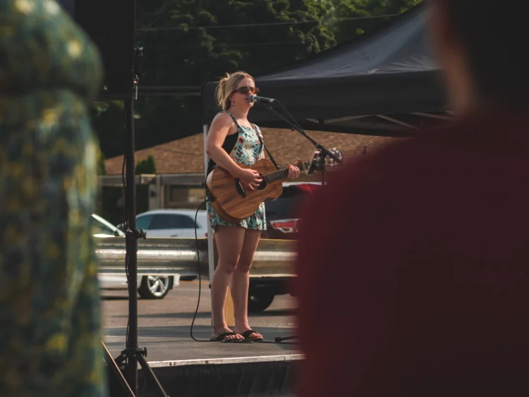 Sarina Haggarty performing live with an acoustic guitar at National Ice Cream Day at Merla-Mae Ice Cream