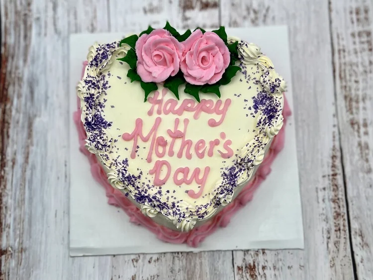 Heart-shaped Happy Mother&rsquo;s Day ice cream cake with two pink icing roses and a purple sprinkle border, on a whitewashed wood table at Merla-Mae Ice Cream in London, Ontario