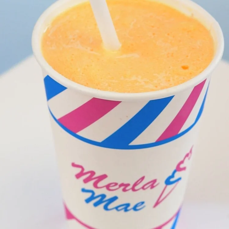 Orange Freezie of slush and vanilla soft-serve with a straw in a striped cup at Merla-Mae Ice Cream in London, Ontario