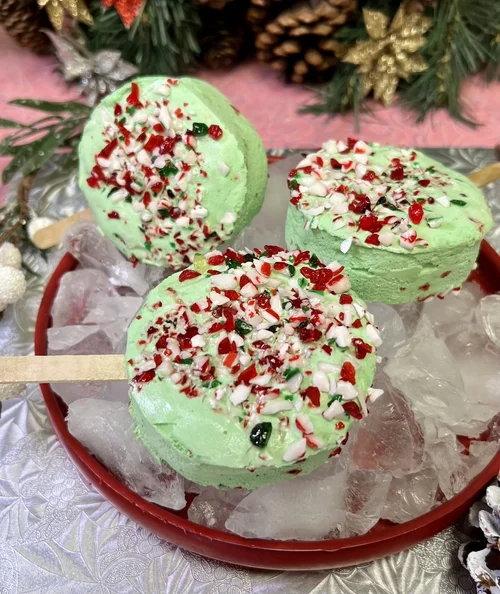 Mint-green ice cream bars on wooden sticks topped with crushed candy cane, with pine branches behind, at Merla-Mae Ice Cream in London, Ontario