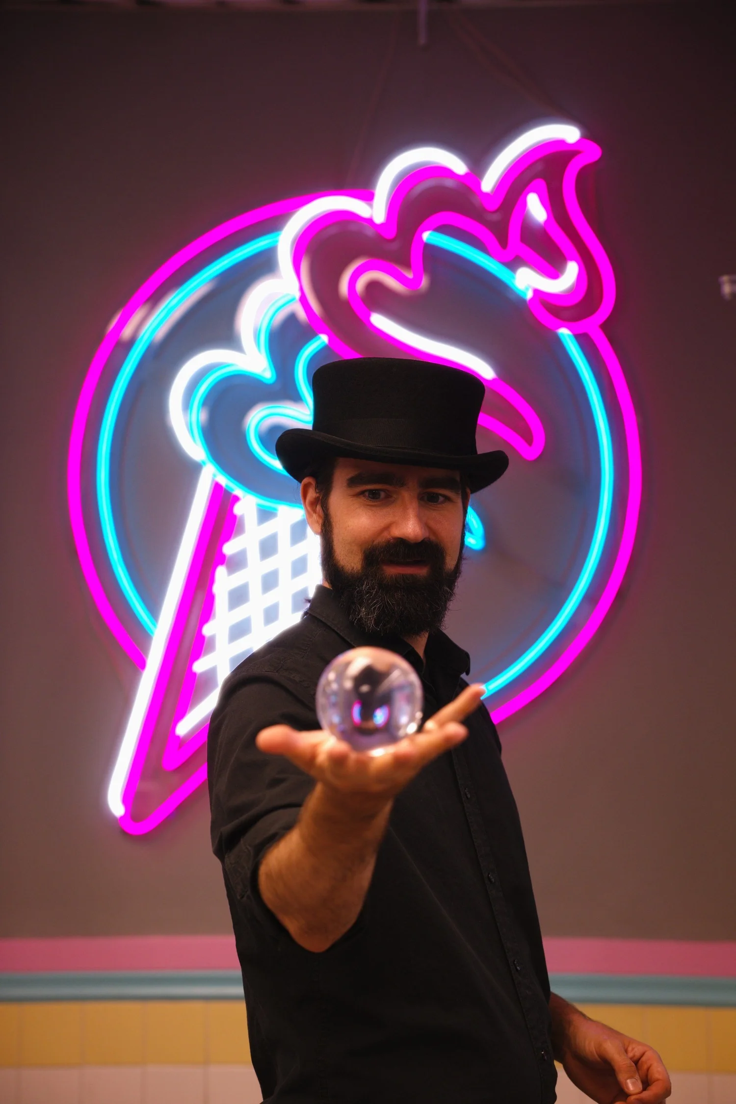 Magician performing with a crystal ball beside the Merla-Mae neon sign