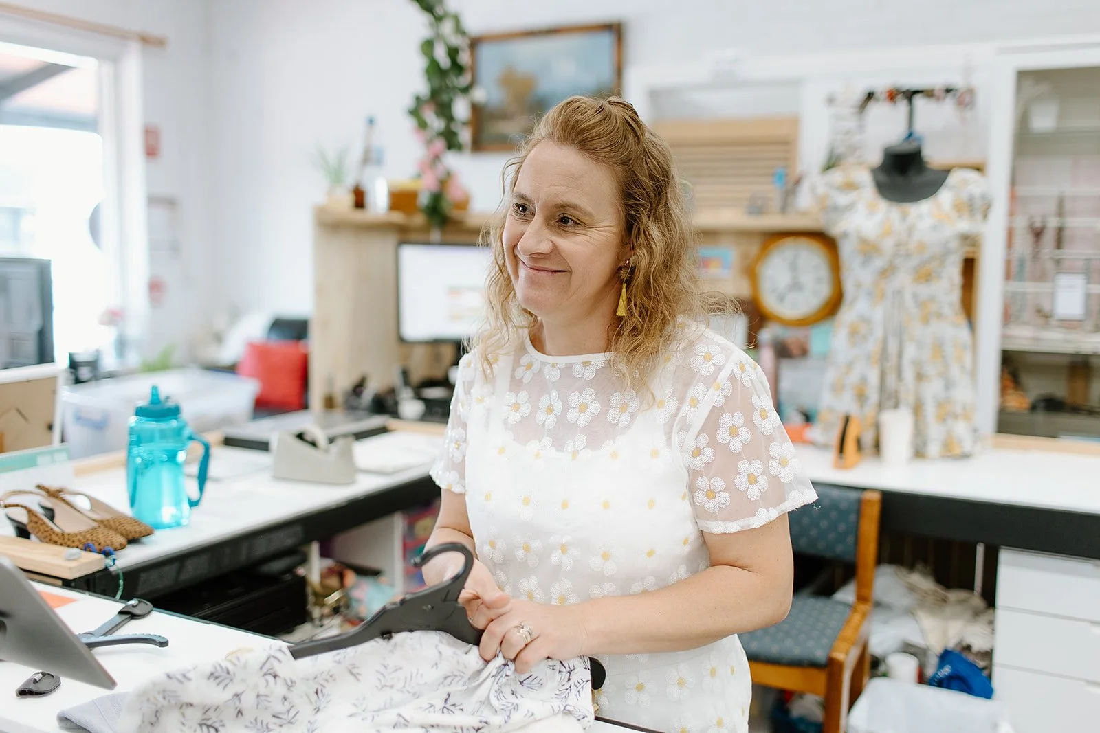 Op shop attendant wearing embroidered top with white and yellow daisies, smiling as she listens to someone
