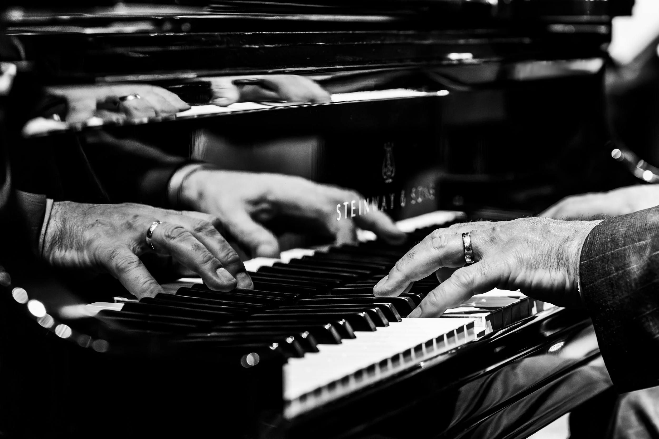 Close-up of hands playing a grand piano in black and white.